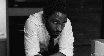 Movie still from “Malcolm & Marie” (2021), directed by Sam Levinson – A black and white photo of a man leaning on a table; Close Up shot, Low angle