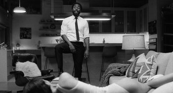 Movie still from “Malcolm & Marie” (2021), directed by Sam Levinson – A black and white photo of a man sitting on a stool; Wide shot, Low angle