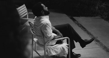 Movie still from “Malcolm & Marie” (2021), directed by Sam Levinson – A black and white photo of a man sitting in a chair; Medium shot, High angle