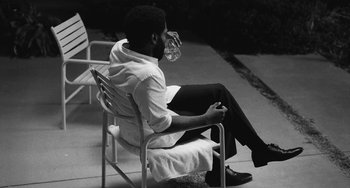 Movie still from “Malcolm & Marie” (2021), directed by Sam Levinson – A black and white photo of a man sitting in a chair; Medium shot, High angle