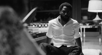 Movie still from “Malcolm & Marie” (2021), directed by Sam Levinson – A black and white photo of a man sitting on a bench; Medium shot, Low angle