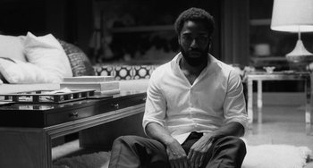 Movie still from “Malcolm & Marie” (2021), directed by Sam Levinson – A black and white photo of a man sitting on a couch; Medium shot, Low angle