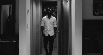 Movie still from “Malcolm & Marie” (2021), directed by Sam Levinson – A man in a white shirt is standing in a doorway; Wide shot, High angle