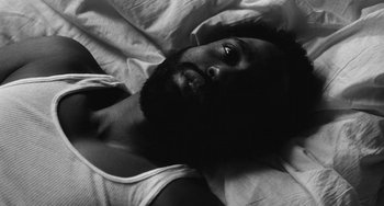 Movie still from “Malcolm & Marie” (2021), directed by Sam Levinson – A black and white photo of a man laying in a bed; Close Up shot, Overhead angle