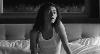 Movie still from “Malcolm & Marie” (2021), directed by Sam Levinson – A young woman sitting on a couch looking at the camera; Medium shot, Low angle