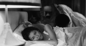 Movie still from “Malcolm & Marie” (2021), directed by Sam Levinson – A woman laying in a bed with a man in the background; Medium shot, High angle