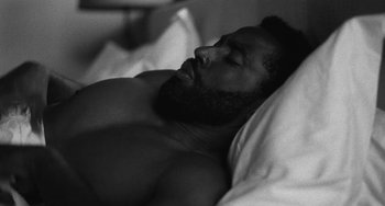 Movie still from “Malcolm & Marie” (2021), directed by Sam Levinson – A black and white photo of a man sleeping in a bed; Close Up shot, High angle