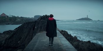 Movie still from “Marianne” (2019), created by Samuel Bodin – A person walking on a pier near the ocean; Wide shot, Over the shoulder angle