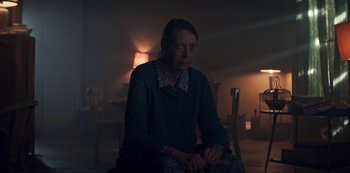 Movie still from “Marianne” (2019), created by Samuel Bodin – An older woman sitting in a dark room; Medium shot, Low angle