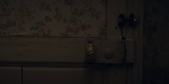 Movie still from “Marianne” (2019), created by Samuel Bodin – A cat sitting on a door in a dark room; Extreme Close Up shot, High angle