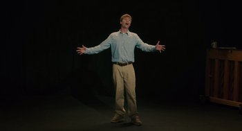 Movie still from “Lady Bird” (2017), directed by Greta Gerwig – A man standing in the dark with his arms outstretched; Medium shot, Low angle