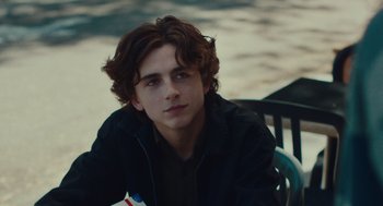 Movie still from “Lady Bird” (2017), directed by Greta Gerwig – A young man sitting at a table with a book in his hand; Close Up shot, Over the shoulder angle