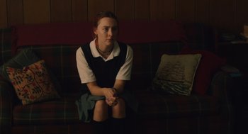 Movie still from “Lady Bird” (2017), directed by Greta Gerwig – A woman sitting on a couch with her hands crossed; Medium shot, High angle