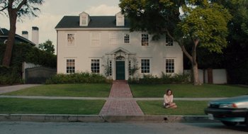Movie still from “Lady Bird” (2017), directed by Greta Gerwig – A woman sitting on the grass in front of a white house; Extreme Wide shot, High angle