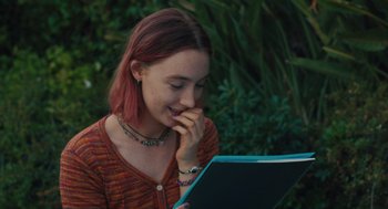 Movie still from “Lady Bird” (2017), directed by Greta Gerwig – A girl with pink hair is reading a book; Close Up shot, Over the shoulder angle