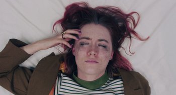 Movie still from “Lady Bird” (2017), directed by Greta Gerwig – A woman with pink hair laying on a bed with her eyes closed; Close Up shot, Overhead angle