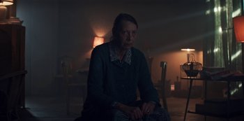 Movie still from “Marianne” (2019), created by Samuel Bodin – An older woman sitting in a dark room; Medium shot, Low angle
