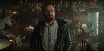 Movie still from “Marianne” (2019), created by Samuel Bodin – A man with a goatee standing in front of a chandelier; Medium shot, Low angle