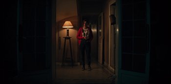 Movie still from “Marianne” (2019), created by Samuel Bodin – A woman standing in a dark hallway holding a cell phone; Wide shot, Low angle
