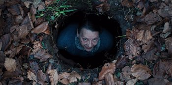 Movie still from “Marianne” (2019), created by Samuel Bodin – A woman in a hole in the ground with leaves around her; Medium shot, Overhead angle
