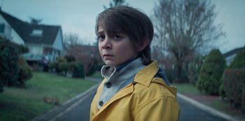 Movie still from “Marianne” (2019), created by Samuel Bodin – A young boy in a yellow raincoat standing on the side of the road; Close Up shot, Low angle