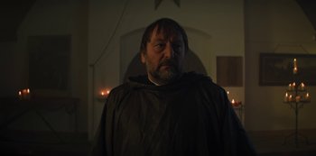 Movie still from “Marianne” (2019), created by Samuel Bodin – A man wearing a black robe standing next to candles; Medium shot, Low angle