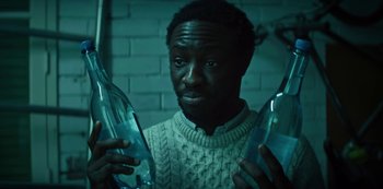 Movie still from “Marianne” (2019), created by Samuel Bodin – A man holding two bottles in his hands; Close Up shot, High angle