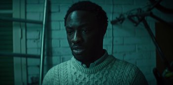 Movie still from “Marianne” (2019), created by Samuel Bodin – A man wearing a sweater standing next to a brick wall; Close Up shot, High angle