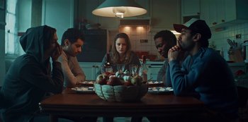 Movie still from “Marianne” (2019), created by Samuel Bodin – A group of people sitting around a table with a bowl of fruit; Medium shot, High angle