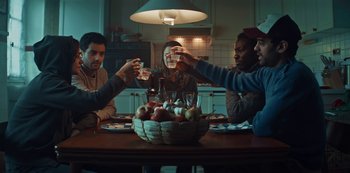 Movie still from “Marianne” (2019), created by Samuel Bodin – A group of people sitting at a table with a bowl of fruit; Medium shot, Low angle