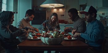 Movie still from “Marianne” (2019), created by Samuel Bodin – A group of people sitting around a table with a bowl of fruit; Medium shot, High angle