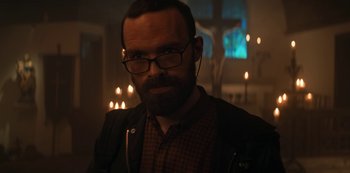 Movie still from “Marianne” (2019), created by Samuel Bodin – A man with a beard wearing glasses in a room; Close Up shot, Low angle