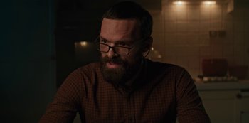 Movie still from “Marianne” (2019), created by Samuel Bodin – A man with a goatee wearing glasses and a plaid shirt; Close Up shot, Over the shoulder angle