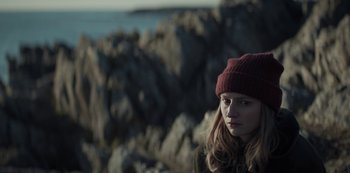 Movie still from “Marianne” (2019), created by Samuel Bodin – A woman wearing a hat standing in front of rocks; Close Up shot, High angle