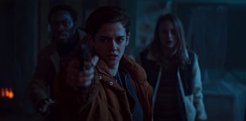 Movie still from “Marianne” (2019), created by Samuel Bodin – A woman holding a gun in a room with other people; Medium shot, Over the shoulder angle