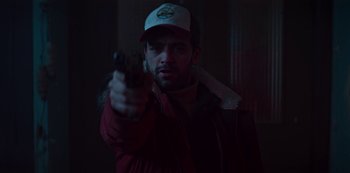 Movie still from “Marianne” (2019), created by Samuel Bodin – A man holding a gun while wearing a baseball cap; Close Up shot, Over the shoulder angle