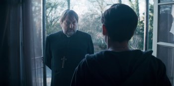 Movie still from “Marianne” (2019), created by Samuel Bodin – A man wearing a priest's outfit looking in the mirror; Medium shot, Over the shoulder angle