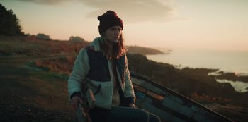 Movie still from “Marianne” (2019), created by Samuel Bodin – A woman sitting on the side of a cliff; Medium shot, Low angle