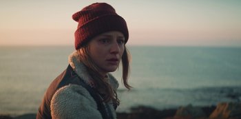 Movie still from “Marianne” (2019), created by Samuel Bodin – A woman wearing a red hat standing next to a body of water; Close Up shot, Over the shoulder angle