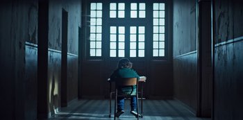 Movie still from “Marianne” (2019), created by Samuel Bodin – A little boy sitting in a chair in front of a window; Wide shot, Low angle