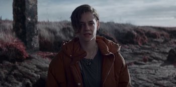 Movie still from “Marianne” (2019), created by Samuel Bodin – A person wearing a brown jacket standing in a field; Medium shot, Low angle