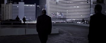 Movie still from “Miami Vice” (2006), directed by Michael Mann – A man in a black jacket is walking in a parking lot at night; Wide shot, Low angle