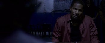 Movie still from “Miami Vice” (2006), directed by Michael Mann – A man sitting at a table in front of a wall; Close Up shot, Over the shoulder angle