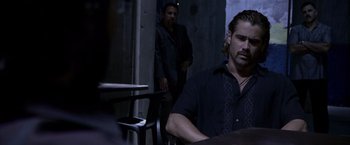 Movie still from “Miami Vice” (2006), directed by Michael Mann – A man sitting at a table in front of another man standing behind him; Medium shot, Over the shoulder angle