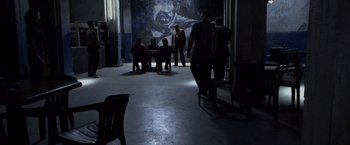 Movie still from “Miami Vice” (2006), directed by Michael Mann – A group of people standing in a room with a painting on the wall behind them; Wide shot, Over the shoulder angle