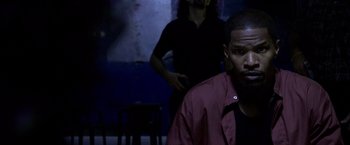 Movie still from “Miami Vice” (2006), directed by Michael Mann – A man in a dark room with another man standing behind him; Close Up shot, Over the shoulder angle