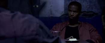 Movie still from “Miami Vice” (2006), directed by Michael Mann – A man sitting at a table with a glass of water; Medium shot, Over the shoulder angle