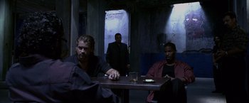 Movie still from “Miami Vice” (2006), directed by Michael Mann – A group of men sitting at a table in a dark room; Medium shot, Over the shoulder angle