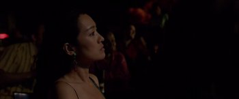 Movie still from “Miami Vice” (2006), directed by Michael Mann – A woman is standing in a dark room with people; Close Up shot, Over the shoulder angle