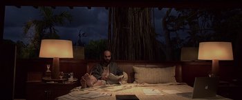 Movie still from “Miami Vice” (2006), directed by Michael Mann – A man sitting on a bed reading a book; Wide shot, Low angle